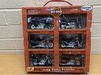 Front view of the boxed set showing six Harley Davidson motorcycle models in compartments, with brown brick-wall style packaging and Harley Davidson logos.