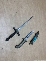 Photo showing all three items: mini dagger letter opener, small knife with engraved blade, turquoise-handled knife letter opener with sheath.