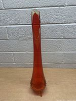 Full front view of tall red glass vase showing shape, color and base feet.