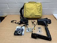 Wide shot showing all items: SeaLife underwater camera in waterproof housing, handheld underwater flash/light, yellow carrying case, cables, accessories, and manual on a table.