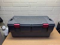 Front view of the large dark gray storage tote with folded lid and red locking clips secured.