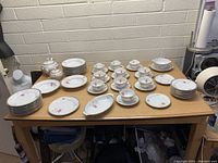 View of the entire china set arranged on a table showing multiple plates, teacups with saucers, serving bowls and teapot with floral pattern.