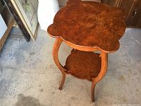Full view of antique burl oak side table showing scalloped edge top and bottom tier with curved legs.