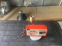 Full view of the Coca Cola radio style lamp showing red rectangular radio-like base on round silver stand with bulb socket and metal harp holder.