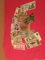 Overview photo showing multiple foreign bills, including Confederate and various international notes spread out on red cloth.