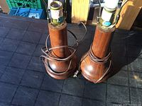 Photo of two matching Mid-Century Modern teak table lamp bases from a top angle, showing the wood grain, electrical cords, and bulb sockets without bulbs installed on one lamp.
