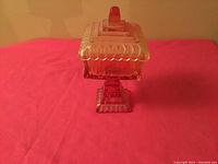Full view of mid century pink glass candy dish with lid on red surface