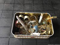 Assorted vintage watches and bands in a decorative tin container on a black grid surface