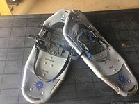 Full view of Powder Ridge snow shoes on a black mat showing the gray frame with blue details and adjustable straps.