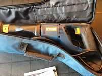 Ryobi brand electric reciprocating saw in blue, black, and orange inside an open black soft carry case with handle. User manual visible below saw.