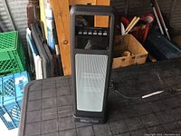 Full view of the black stand-up ceramic tower heater with front mesh grille and control panel on top