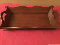 Top view of vintage solid cherry wood bread tray with scalloped sides and cut-out handles on red cloth background.