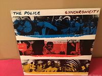 Front side of the Synchronicity album cover showing photographic strips in blue, red, and yellow with band images and "The Police Synchronicity" text.