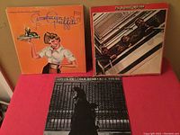 Three vintage rock vinyl LP covers displayed on a pink surface: American Graffiti soundtrack, The Factory, and Neil Young albums visible.