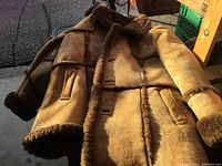Full front view of tan suede sheepskin coat laid flat showing exterior and pocket placement