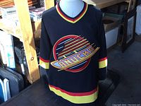 Full front view of the black Vancouver Canucks hockey jersey with colorful stripes and large emblem
