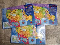 Three boxed GeoPuzzle magnetic puzzles of the USA, each showing colorful maps and packaging with educational themes.