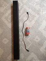 Top-down view of the black sound bar next to a soda can for size reference, with a power cord laid out beside it.