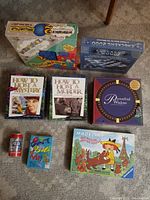 Seven vintage board games in shrink wrap arranged on a carpet, showing How to Host a Mystery, How to Host a Murder, Proverbial Wisdom, Chess 2000, Polar Soda mini game, Don't Bug Me!, and a Madeline game.