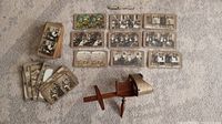 Antique stereoscope with large collection of black and white stereoscopic slides laid out on carpet.