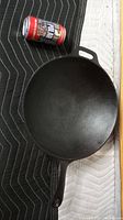 Top-down view of black cast iron skillet beside a standard soda can for size comparison on a padded moving blanket.