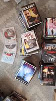 Photo showing stacks of DVDs in cases on carpet. Titles visible include The Soloist, The Town, Last Man Standing, among others.