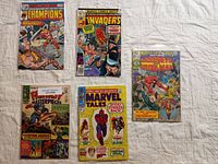 Photo showing five Marvel comic books laid flat on a white textured surface. Titles visible include The Champions, The Invaders, Marvel Super-Heroes Daredevil and Iron Man Giant-Size, Lord of Light Masterpieces, and Marvel Tales.