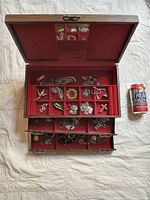 Open wooden jewelry box showing multiple compartments filled with assorted costume jewelry pieces including brooches, earrings, pendants, and pins.