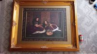 Full view of the large painting set in an ornate golden frame, showing two young women indoors, one holding a goldfish bowl, with a soda can for scale.