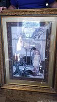 Framed painting held by a person showcasing the child subject and ornate frame with reflections visible on the glass.