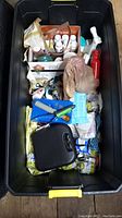 Large black plastic tote filled with assorted dog grooming supplies including spray bottles, gloves, towels, and grooming accessories.