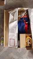 Madonna doll in blue and red outfit with gold halo, laid in original packaging along with the certificate of authenticity and care sheets.
