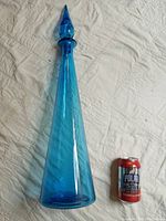 Tall blue blown glass bottle next to a standard soda can for size reference.