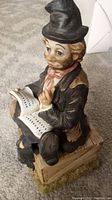 Porcelain clown figurine detailed side view showing the clown holding an open music book and seated on crate base