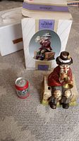 Photo showing the figurine seated on a wooden crate with a trumpet, in front of the original Melody In Motion box, with a soda can next to it for scale.