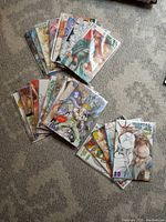 Top-down view of all 24 comics fanned out on a carpeted floor, showing colorful covers and plastic bag protection.