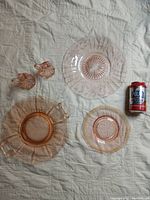 Five pink glassware pieces displayed on a quilted white surface. Includes small handled creamer and sugar bowl, small starburst patterned plate, medium plate with gold detailing and a large platter with some gold wear.