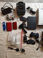 Overhead view showing GameCube console, controller, power brick and AV cable alongside PS2 Slim, Xbox 360, power cables and controllers