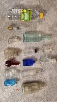 Photo of all 11 antique bottles and 2 additional items arranged on carpet, showing various colors, shapes, and sizes including a water bottle for scale.