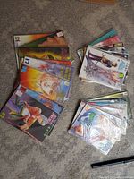 Photo showing stacks of The Blood Sword comics issues 1-23 laid out on carpeted floor. Comics are bagged in plastic sleeves. Visible are various cover illustrations depicting characters and action scenes from the series.