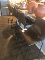 Four dark brown faux leather bar stools lined up at a kitchen counter with metal legs and footrest bars.