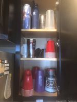 Kitchen cabinet shelves with various drinkware including plastic cups, insulated bottles, metal mugs, and a stack of red Solo cups.