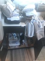 Stacked bath towels, bath rugs and linens on bathroom cabinet and counter including white, gray, beige and black towels.