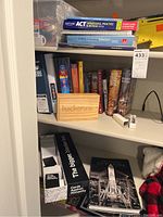 View of shelf with educational books, board games, and card games including Kaplan ACT prep book, Usborne book, strategy books, wooden hackerone box, and various game boxes.