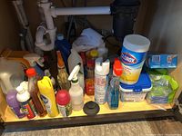 Cleaning products stored under the kitchen sink, showing assembled bottles and containers.