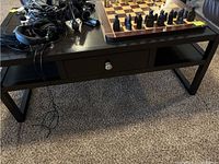 Full view of black wood coffee table with various items on top (not included) showing legs and drawer.