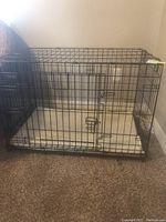 Front angle view of the metal wire dog crate on carpeted floor showing the door latches and removable tray base.