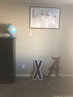 Wide shot showing the globe, framed basketball poster on the wall, and two large letter signs 'X' and 'A' on the floor.