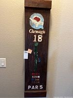 Full view of wooden golf art panel showing Gleneagle logo, hole number, golf bag, and yardages, with labels and wall background.