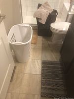 White tall hamper near bathroom door on beige tiled floor